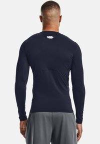 Marineblå langermet treningsskjorte laget av elastisk materiale. Har en tettsittende fasong og en liten logo på øvre rygg. Minimalistisk design.