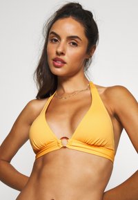 Gelber Bikini-Oberteil mit dreieckigem Design, ausgestattet mit einem Vorderdreh-Detail und einem runden, braunen Akzent. Glatter Stoff mit verstellbaren Trägern.