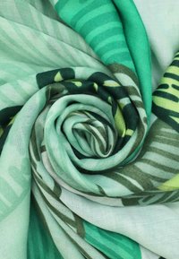 Tessuto verde a motivo, arrotolato in una spirale, con un mix di righe e foglie, caratterizzato da una consistenza morbida e leggera.