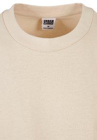 T-shirt en coton beige avec un col rond classique. Présente une texture simple et lisse ainsi qu'une étiquette discrète à l'intérieur. Taille moyenne.