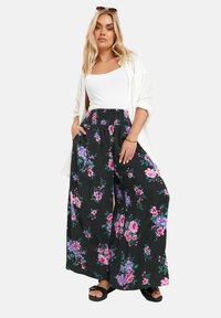 Svarta blommiga vida byxor med lila och rosa blomstermönster, med en smockad midja och sidofickor. Matchat med en vit linne.