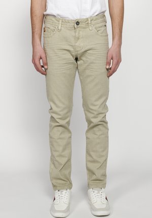 Light beige slim-fit jeans with a smooth texture, five-pocket design, and subtle stitching details, worn with white sneakers.
