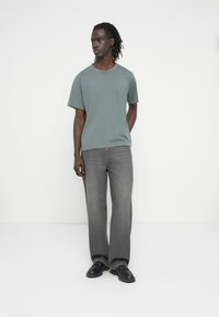 Ανοιχτό πράσινο βαμβακερό t-shirt με κοντά μανίκια, συνδυασμένο με γκρι τζιν φαρδιάς γραμμής και μαύρες μοκασίνες. Απλός σχεδιασμός, ομαλή υφή.