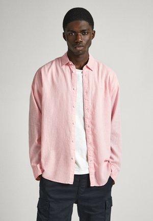 Camisa de lino de manga larga en color rosa claro con botonadura frontal y un corte relajado, superpuesta a una camiseta blanca básica.