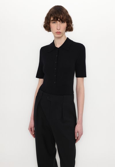 Polo noir en maille côtelée avec des manches courtes, doté d'un col et d'une rangée de boutons. Associé à un pantalon tailleur noir taille haute.