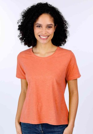 Short-sleeve, round-neck T-shirt in coral hue. Made from soft fabric with a slight heathered texture. Paired with denim, displayed on a model.