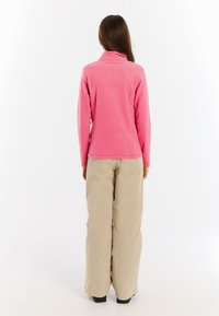 Roze fleecejack met hoge kraag, lange mouwen en een gladde textuur, gecombineerd met losse beige broek.