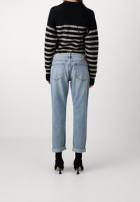 Suéter a rayas negro y beige, jeans de tiro alto azules claros con dobladillos, combinados con zapatos de tacón negros.