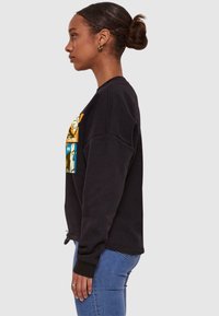 Czarny sweatshirt o luźnym kroju, z kolorową grafiką z kreskówki na klatce piersiowej. Żebrowane mankiety i regulowany sznurek u dołu.