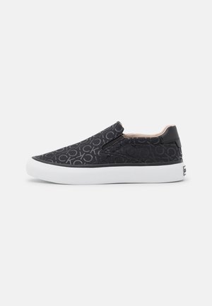 Czarny sneaker typu slip-on z powtarzającym się wzorem "CK", biała gruba podeszwa i niski krój przy kostce.