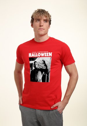 Rød bomulds T-shirt med et sort og hvidt grafisk print af en maskeret figur med teksten "JOHN CARPENTER'S HALLOWEEN" ovenfor.
