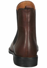 Bota Chelsea de cuero marrón con paneles laterales elásticos negros, punta redondeada y tacón bajo negro. Presenta una textura suave y detalles de costura mínimos.