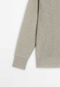 Pull en tricot gris clair avec un motif texturé, des poignets côtelés et une coupe décontractée. Présenté partiellement, montrant une manche.