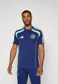 Plava sportska majica od rastezljivog materijala, sadrži svijetloplave naglaske, okrugli izrez na vratu i grb na prsima te kratkim hlačama.