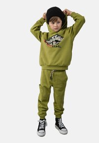 Zielona bawełniana bluza z kapturem z grafiką, dopasowane spodnie dresowe i czarne sneakersy za kostkę. Posiada regulowany kaptur i kieszenie.
