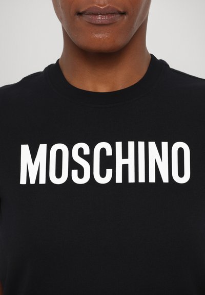 Melnas kokvilnas t-krekls ar izteiksmīgu baltu "MOSCHINO" tekstu krūtīs. Noapaļota kakla izgriezne ar īsām piedurknēm. Gluda tekstūra.