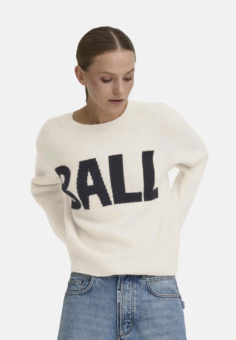 Pull en tricot crème avec un grand graphisme "BALL" en navy. Col rond, texture côtelée et coupe décontractée. Ensemble porté avec un jean en denim bleu.