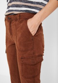 Brown cotton cargo pants featuring side pockets, a smooth texture, and a relaxed fit. Stitch detailing enhances the garment's design.