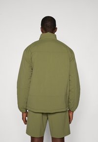 Khaki jacket with a high collar, padded design, and drop shoulders. Matched with shorts in the same fabric and color, minimal seams.