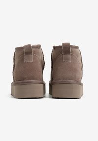 Brązowe zamszowe botki do kostki z grubą podeszwą i pętelką z tyłu. Miękka faktura, brak widocznych wzorów, minimalistyczny design.