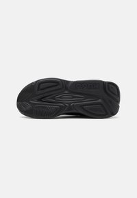 Semelle de chaussure en caoutchouc noir avec motifs de grip texturés et le nom de la marque "HUGO" embossé près de la zone du talon.