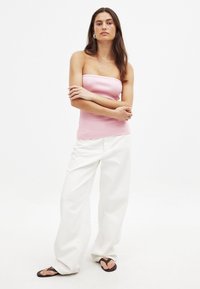 Ljusrosa, axelbandslös topp i ribbad tyg, kombinerad med vita, löst sittande byxor och svarta flip-flops. Enkelt design, inga mönster.