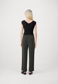 Sorte, tettsittende topp med korte ermer, parret med løse, mørkegrønne bukser. Buksene har elastisk liv. Enkel, moderne design.