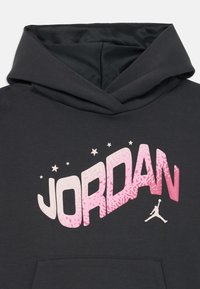 Sötét szürke kapucnis pulóver nagy, rózsaszín és fehér "JORDAN" grafikával és csillag díszítéssel. Tágas kapucnival és puha tapintással rendelkezik.