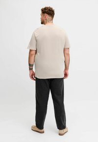 Løsbevægelig beige t-shirt med korte ærmer, kombineret med mørkegrå bukser. Stoffet virker blødt med en glat tekstur.