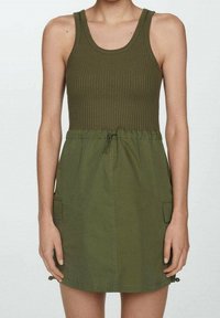 Olivově zelené šaty na ramínka s ribbovaným vrškem, s úzkým pasem a šňůrkou. Obsahuje přední kapsy a přímý střih sukně. Materiál z bavlněné směsi.