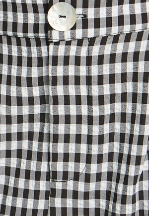 Tissu à carreaux vichy noir et blanc avec une texture lisse, présentant un grand bouton en argent et un détail de poche cousue.