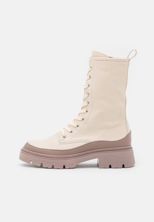 Botte mi-mollet couleur crème à lacets avec une semelle épaisse marron et un bout arrondi sur un fond blanc uni.