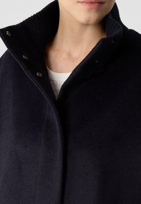 Marineblauer Wollmix-Mantel mit geripptem Stehkragen, Druckknöpfen und weicher Textur, der ein schlankes Design und minimale Details präsentiert.