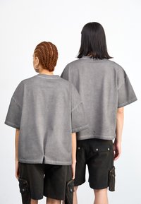 Dos personas visten camisetas de algodón gris de gran tamaño con hombros caídos, combinadas con pantalones cortos de carga oscuros que tienen bolsillos con cremallera.