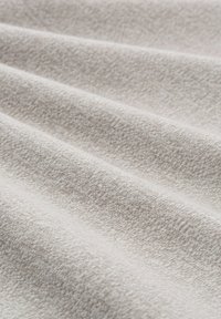 Weiches, hellbeiges Gewebe mit feiner Strickstruktur und sanften Falten, die ein wellenartiges Muster erzeugen.