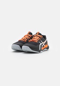 Baskets de sport noires avec des lacets et des accents oranges, présentant une surface texturée, un détail de logo blanc et un design de semelle structurée.