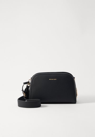 Sac à bandoulière en cuir noir avec surface texturée, quincaillerie dorée, fermeture zippée et bandoulière amovible. Présente un logo embossé sur le devant.
