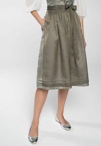 Een satijnen olijfgroene rok met een gestructureerde afwerking, van taille voorzien van een riem, met zijzakken en een zoom met een subtiele glans. Zilveren flats maken de look compleet.