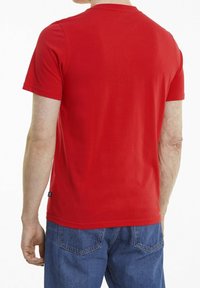 Rød bomulds T-shirt med korte ærmer og rund halsudskæring, med en glat tekstur og let buet kant, båret med blå jeans.