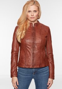Braune Lederjacke mit hohem Kragen, vertikalen Nähten, Reißverschluss vorne und tailliertem Design. Getragen mit blauen Jeans.