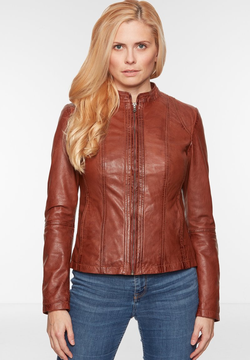 Braune Lederjacke mit hohem Kragen, vertikalen Nähten, Reißverschluss vorne und tailliertem Design. Getragen mit blauen Jeans.