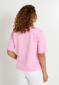 Top de manga corta en color rosa, fabricado con una tela suave, que presenta un corte relajado y un diseño sencillo, con una textura lisa y sin adornos visibles.