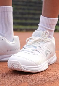 Weiße Tennisschuhe mit Mesh-Obermaterial, abgerundetem Zehenbereich und strukturiertem Sohlenprofil. "HEAD"-Logo an der Seite; die Schnürsenkel sind gebunden, kombiniert mit weißen Socken.