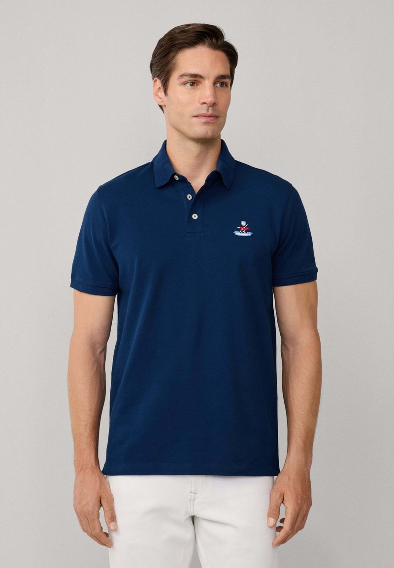 Polo en bleu marine fabriqué en coton, avec un col, des manches courtes et un logo brodé sur la poitrine.