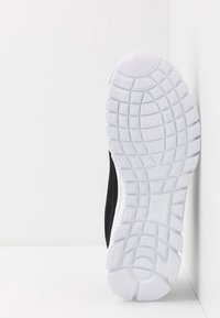 Zapatilla deportiva negra con parte superior de malla texturizada, presenta una suela de goma blanca con un dibujo en la banda para mayor agarre y durabilidad.