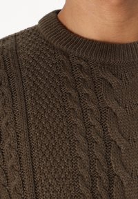Suéter de punto marrón con diseño de cable texturizado y cuello de canalé, que muestra una combinación de complejos patrones de puntadas.