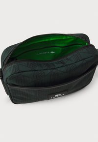 Custodia zip nera e verde realizzata in tessuto con motivo, dotata di un interno foderato in un brillante verde e un'etichetta con logo.