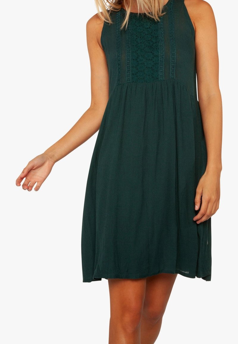 Robe sans manches vert foncé longueur genou avec panneau avant brodé, portée par une personne montrée du cou aux genoux sur fond blanc.