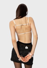 Witte bh met bandjes en metalen accenten, gecombineerd met een zwarte textuur minirok. Model heeft doorzichtige manchetten om de polsen.