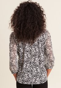 Schwarz-weiße Bluse mit floralem Muster, durchsichtigen Ärmeln und gerafften Manschetten; hat einen abgerundeten Saum und eine lockere Passform.